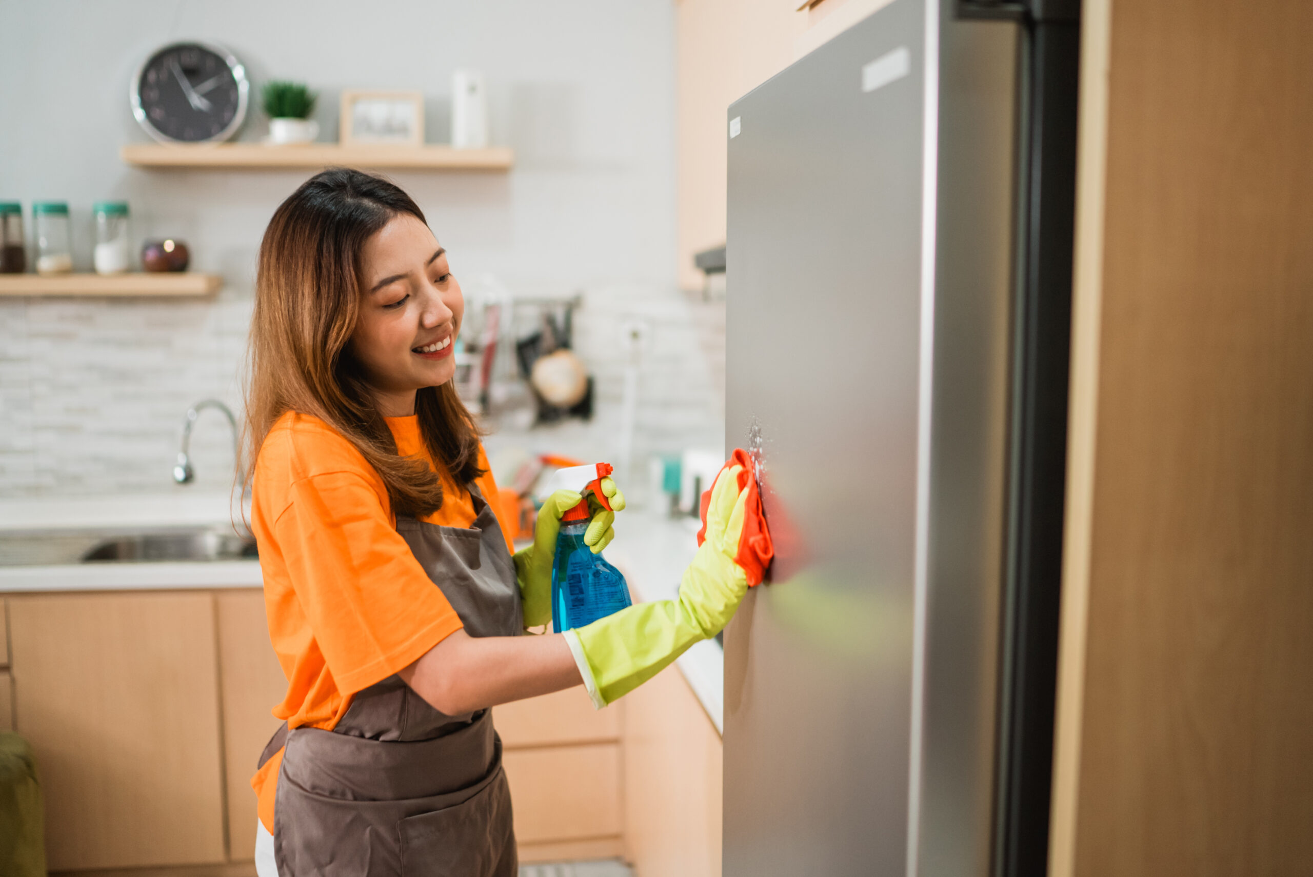 asian woman cleaning refrigerator surface with rag in the kitchen